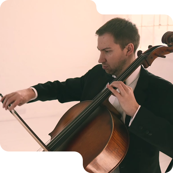Man in a black suit playing a wooden cello with focused expression in a light room.